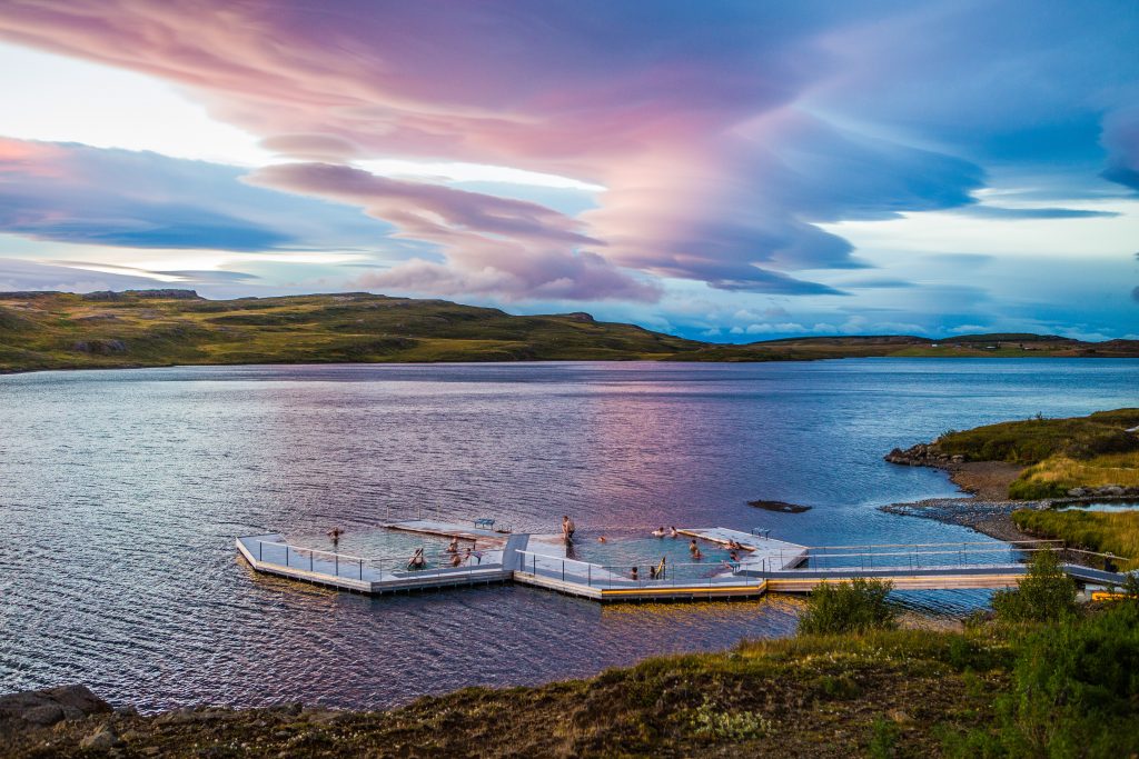 Wide angle view of people in the floating Vok Baths during a dramatic purple and pink sunset.