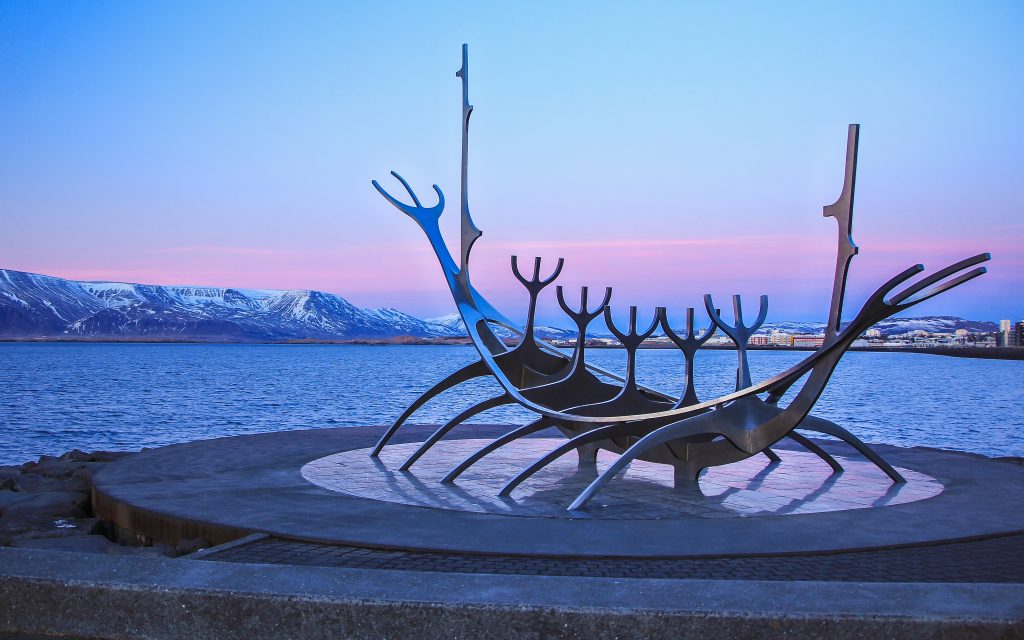 the viking sculpture of the sun voyager viking ship at sunset with the water and mountains in the background