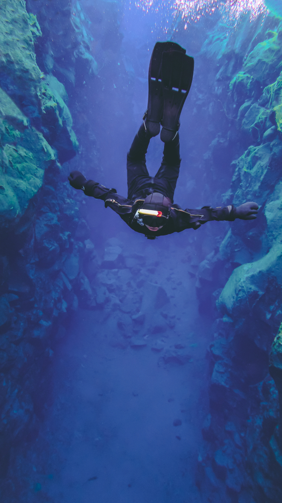 a man scuba diving the Silfra Fissure surrounded by rocks