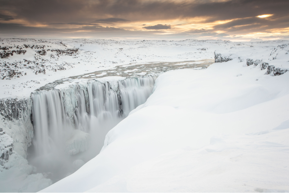 Iceland waterfalls during winter with snow covered banks and mountains under a moody morning sky