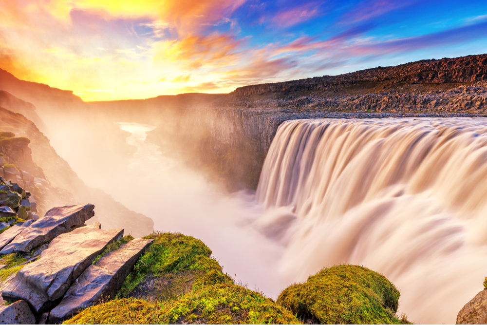 Colorful sunset over West Dettifoss waterfall with roaring waters creating mist within the canyon 
