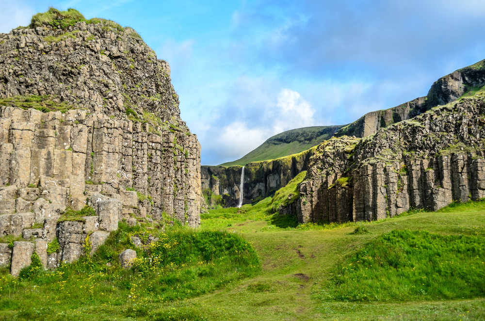 View through the Dwarf Rocks of South Iceland to the distant waterfall with green grass and yellow flowers.