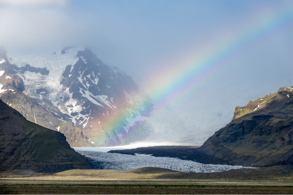 Colorful rainbow covering a glacier outlet with snowy mountains close by