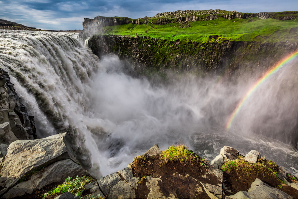 Rainbow beside Europe’s most powerful rushing waterfall lined by a basalt canyon and neon green moss where Prometheus movie was filmed in Iceland