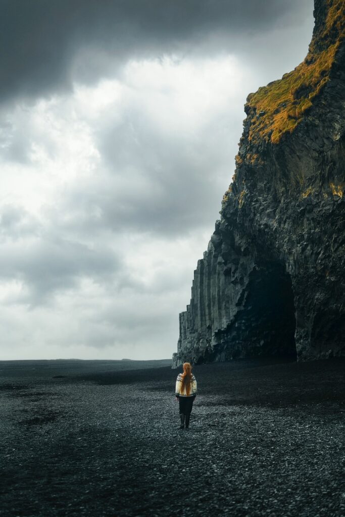 A person in black pants and an Icelandic sweater walking on a black sand beach like one you'd find from Reykjavik to Vik. 