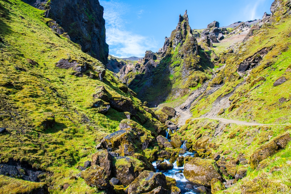 Green and craggy landscape of Thakgil on a sunny day with a stream running through it.