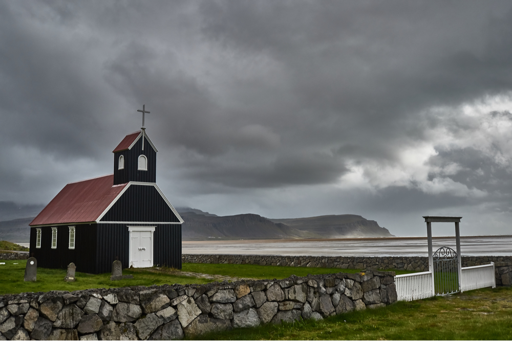 Rauðasandur Church is black with white trim and a red roof and has a graveyard beside it near Rauðasandur Beach