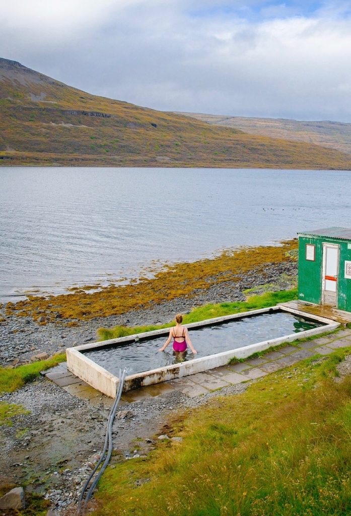 Girl in Hörgshlíðarlaug hot spring with small shed beside during Iceland’s fall months 