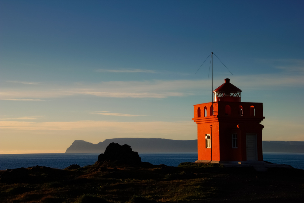 Small orange Svalvogaviti lighthouse offers a beautiful sunset view after a day tour around the westfjord alps
