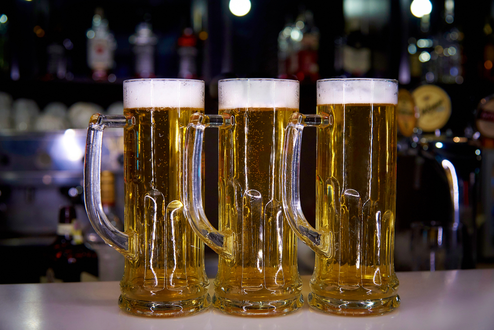 Three mugs with a cold beer on the background of a blurry bar.