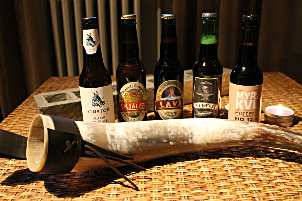 Several bottles of Icelandic beer and a drinking horn displayed on a straw table in an article about beer in Iceland 