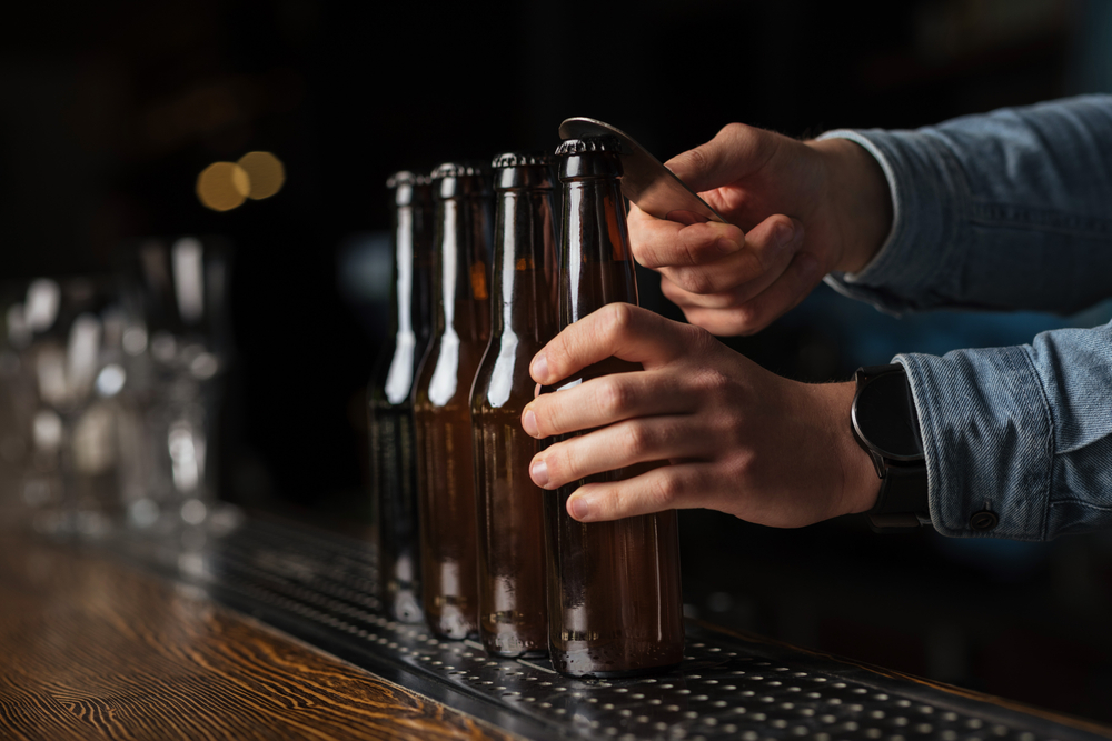 Bartender in jeans shirt opens many bottles  without label on bar counter on blurred background, close up