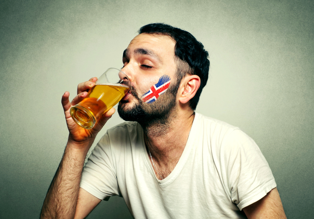 Funny sport fan with flag painted on face drinking a pint.  