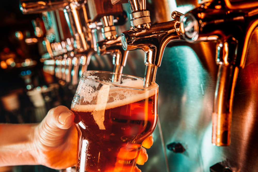 Hand of bartender pouring a large pint  in tap. Bright and modern neon light, males hands.  Side view of young bartender pouring a pint while standing at the bar counter.