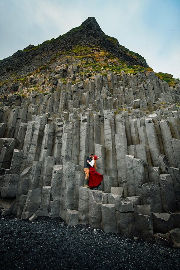 Two people kissing while they are standing on black basalt columns. 