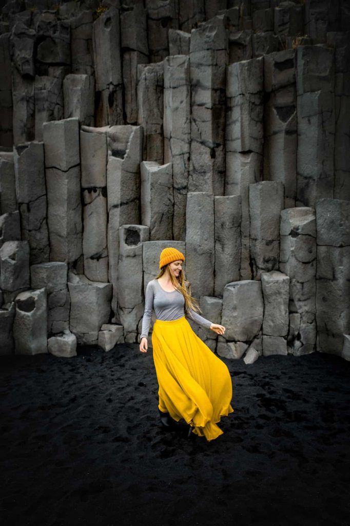 a girl in yellow skirt is standing on black beach 