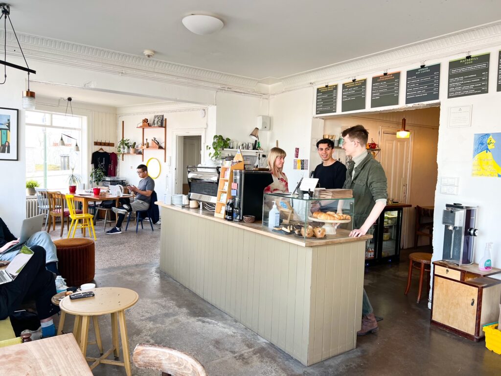 Three people behing the counter of a coffee shop in Iceland and one person sat at a table  