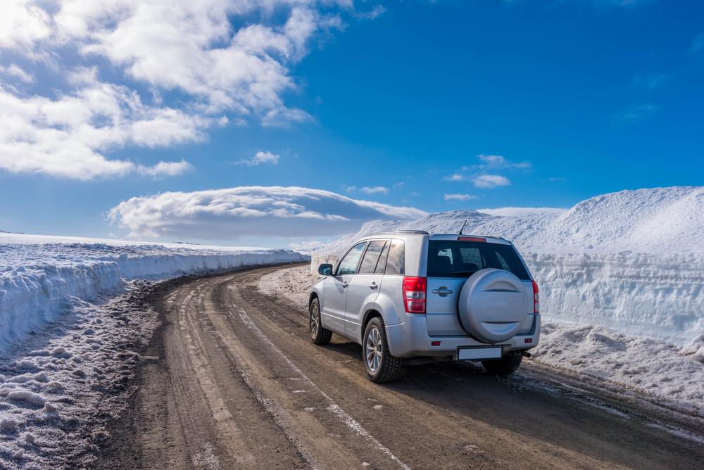 A silver vehicle driving up a road surrounded by snow from Reykjavik to Vik. 