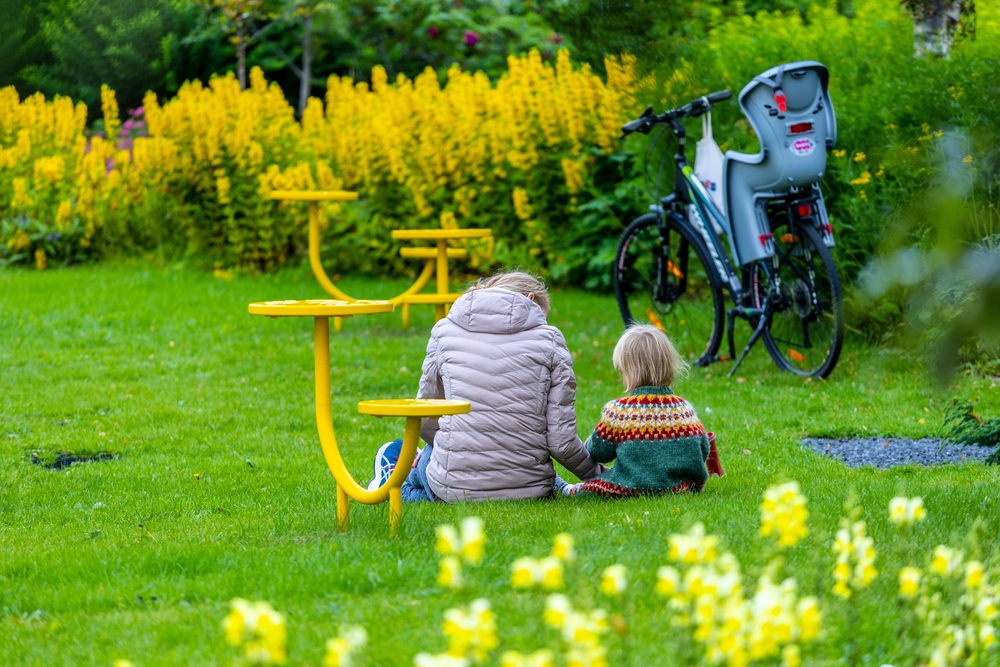 Reykjavik, Iceland mother and child are siting together at local park showing affection towards each other. There are yellow flowers and play eqioment. 