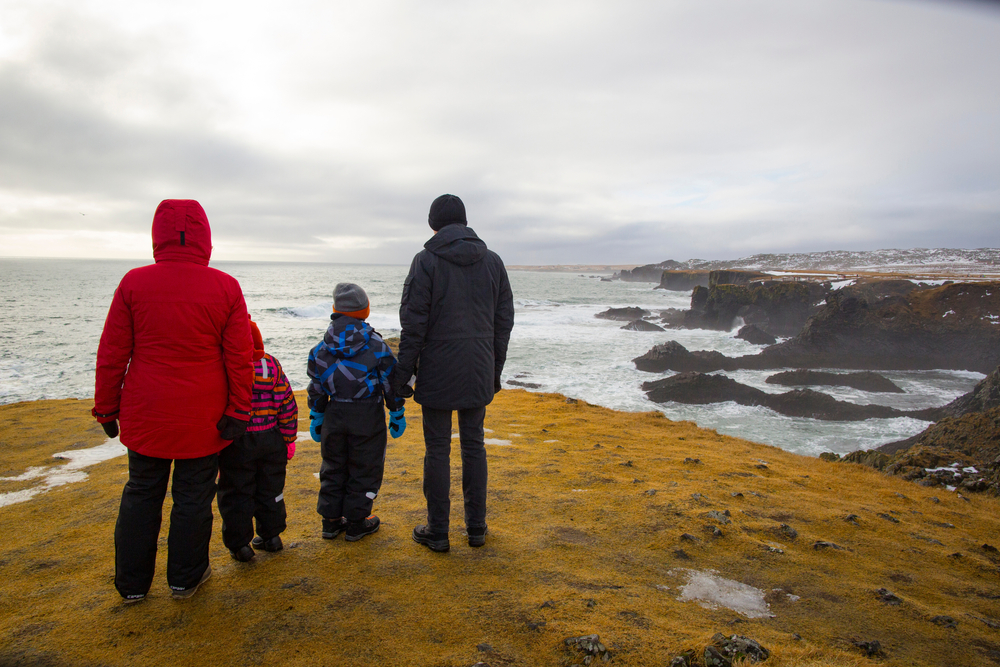 family of tourists visiting Snæfellsnes in Iceland. It is a family of four with two children and they are looking out over the sea from a cliff. Iceland with kids really is a treat