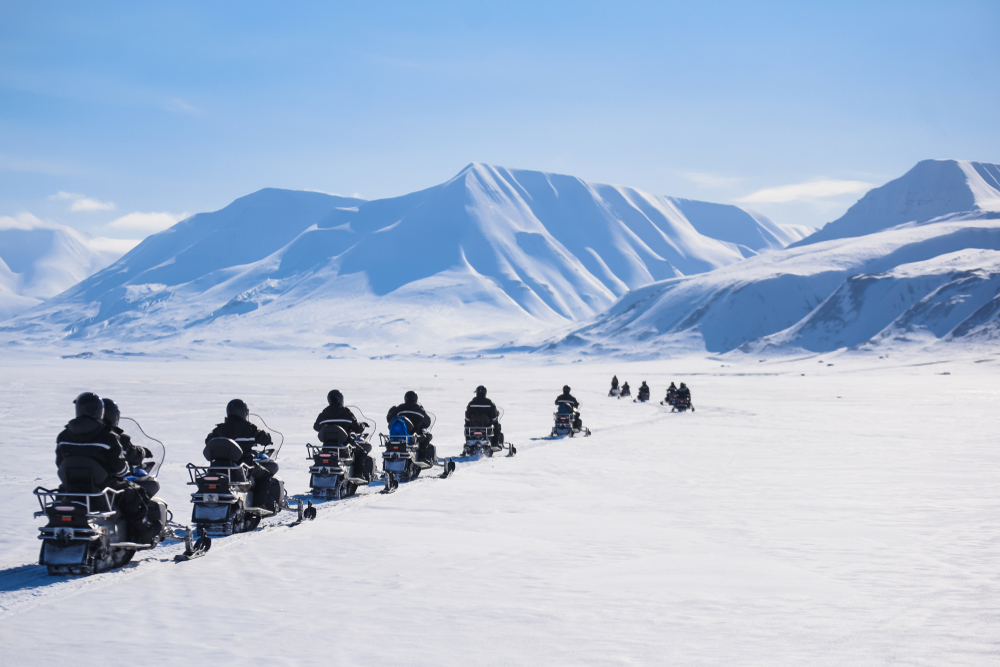 A series of group members drive along snow and toward mountains on ATVs during one of the popular Iceland south coast tours. 