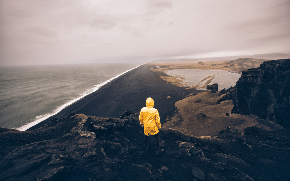 A person in a yellow wind breaker looks out over the black sand beaches during one of those Iceland south coast tours. 