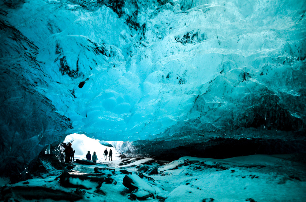 A group from one of the many Iceland south coast tours linger at the entrance of the blue ice caves in Iceland. 