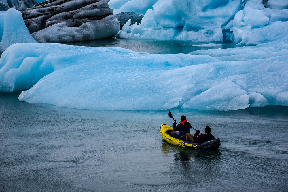 A group of tourists approach a large glacier in a yellow kayak during one of the most popular Iceland south coast tours. 