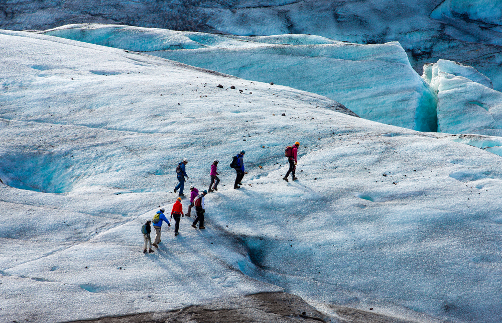 An overhead photo shows a group from one of the Iceland South coast tours walking and hiking over large sections of ice and glaciers. 