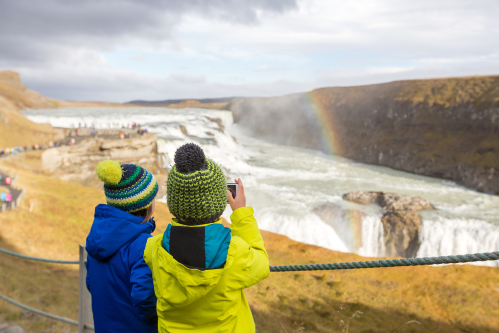 Two children taking a picture of Gullfoss Waterfall. One of things to do in Iceland with kids. 