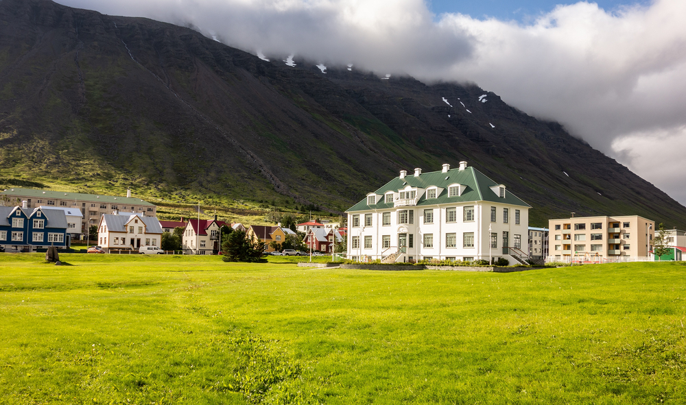  White Isafjordur Culture House on a green meadow at sunny day with storm coming in an article about museums in Iceland. 