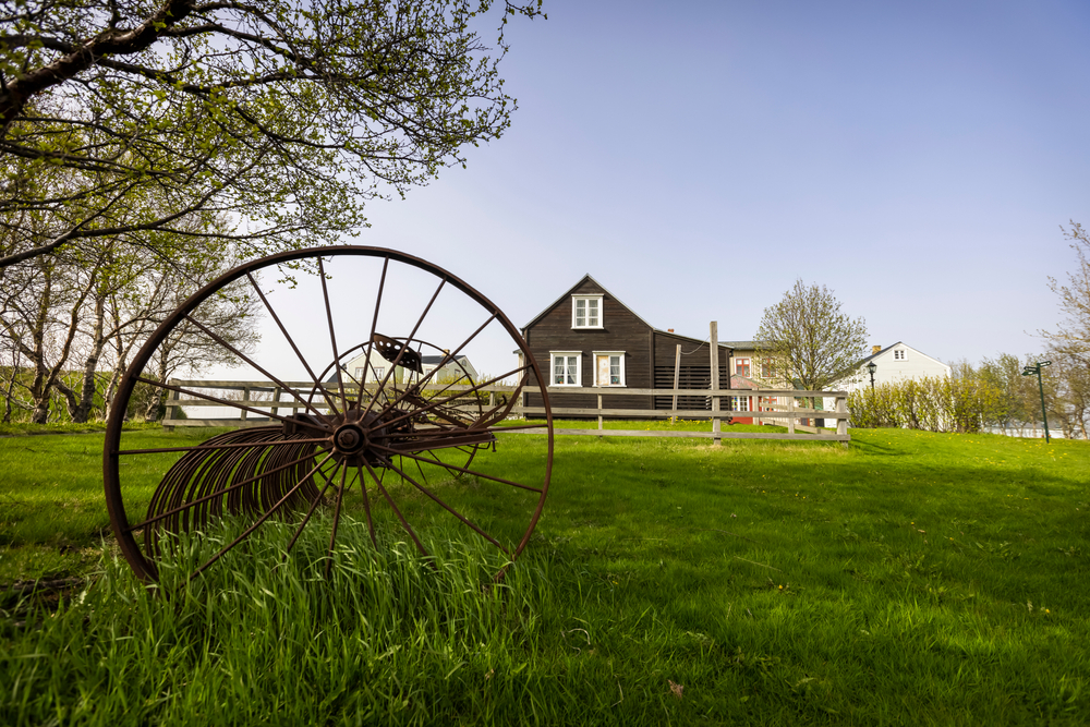 Arbaer open-air museum showing some farming equipment in the foreground and a house in teh background.