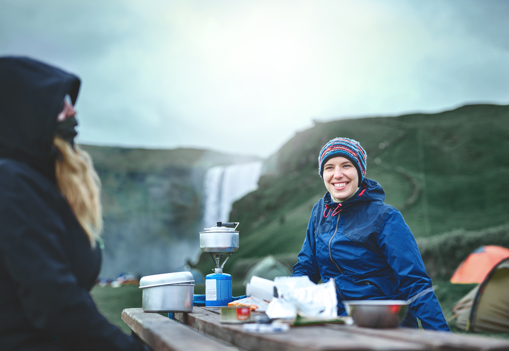 Two people sitting at a picnic table enjoying a packed lunch with a waterfall in the background. 