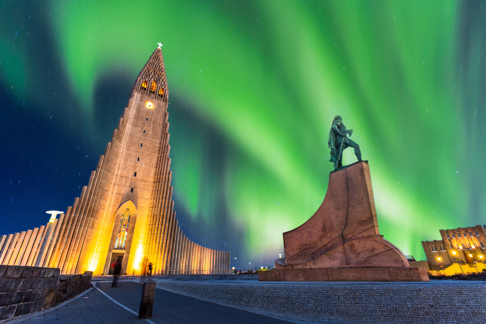 The large church in the center of Reykjavik with the northern lights glowing green in the sky. 