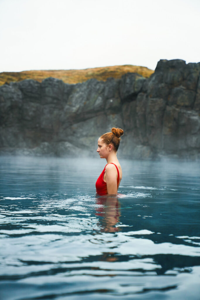 The steam coming off the water surrounded by rocks in the lagoon is a girl swimming in red swimsuit
