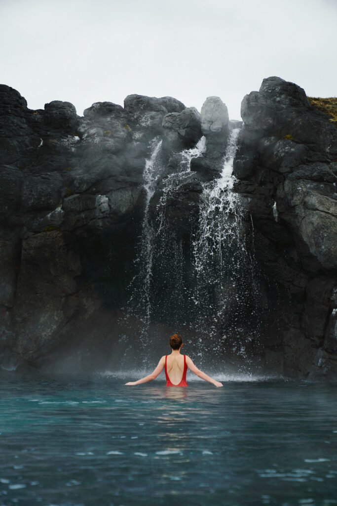 woman standing in front of waterfall at the sky lagoon spa in iceland