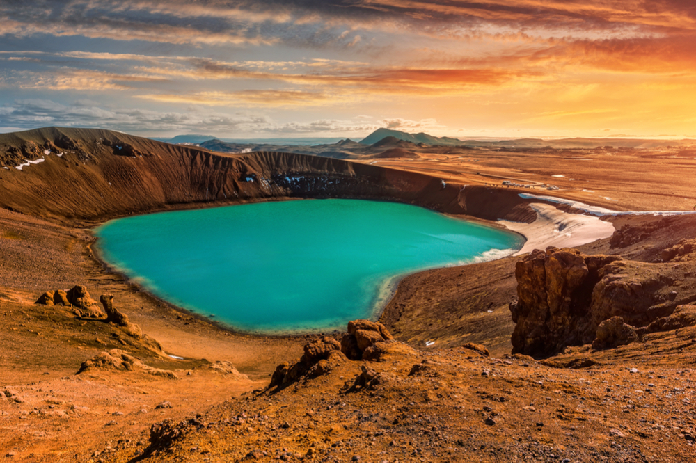 Blue lake in Vito crater surrounded by rocky lands with distant mountains at sunset shown in movies filmed in Iceland