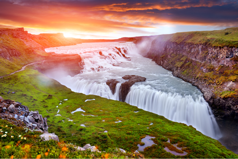 Colorful setting sun and cascading waterfalls spilling into a wide canyon during summertime  is an iceland film locations