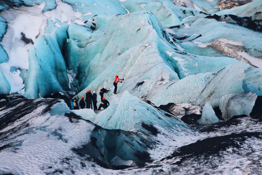 a small group of travelers attempt to use ice axes to scale the Solheimajokull glacier on a tour