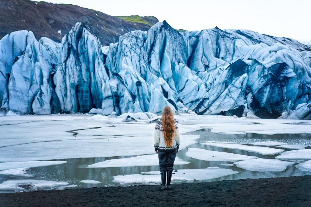 Girl looking at the Shrinking glacier in south Iceland with massive blue and black ice cap ahead