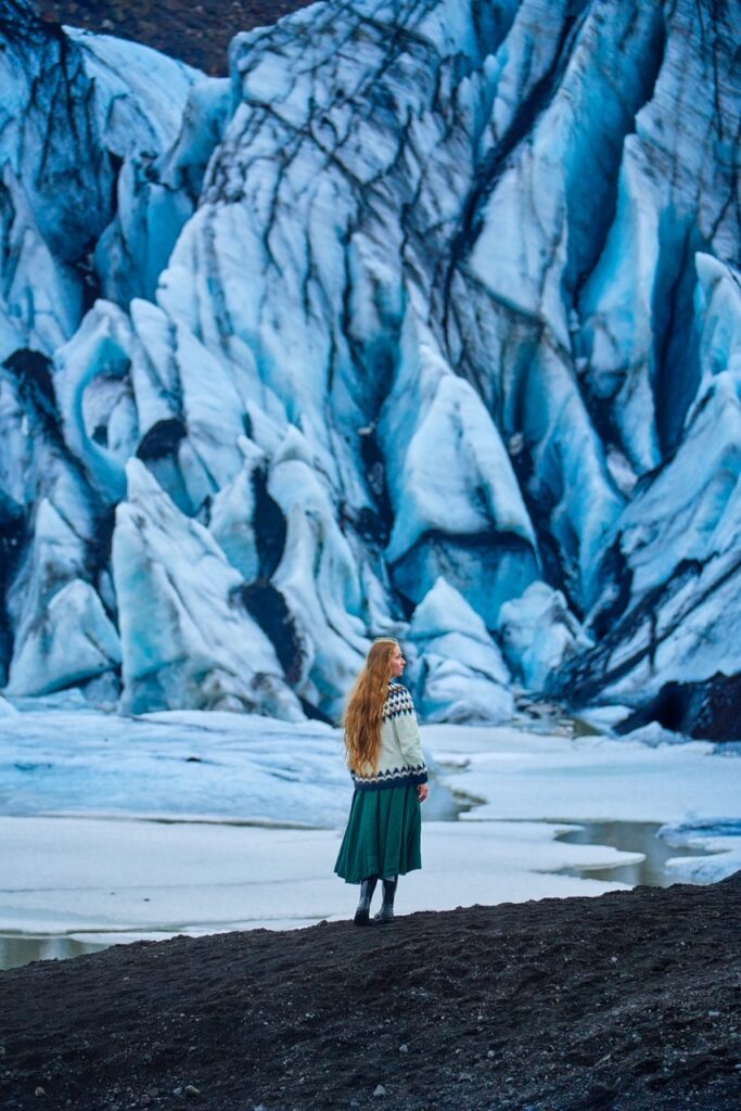 Girl with sheep sweater standing at the base of huge south Iceland glcaier outlet.