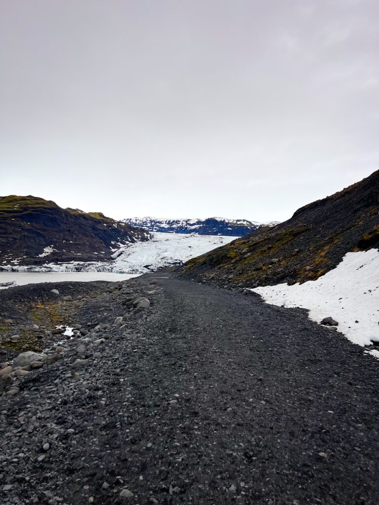 On a moody day, this gravel road off ring road, route 1, is seen with Solheimajokull glcaier lagoon to the left and the glacier outlet ahead.