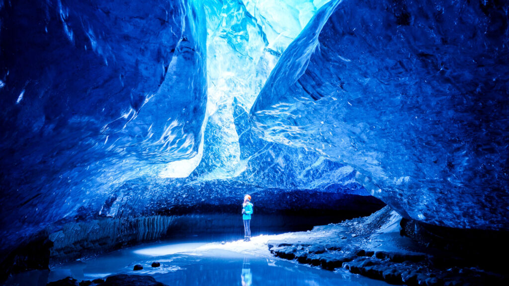 Girl stands looking up to beautiful light show through the glassy blue ice caves in Iceland