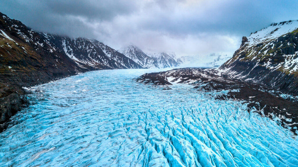 Bright blue glacial outlet flows between moss covered mountains where crystal ice caves in Iceland can be found