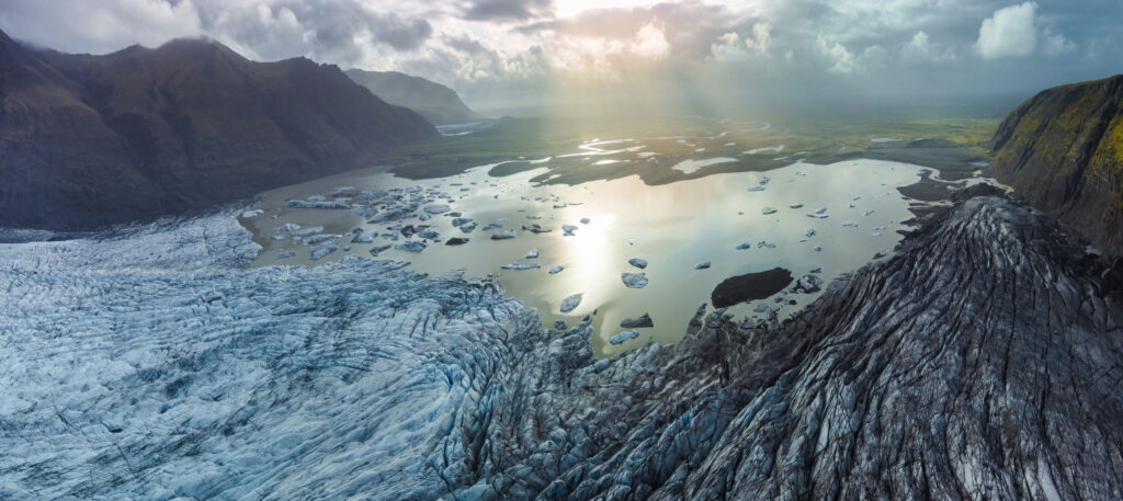 Light bursts through the cloudy skies over Jokulsarlon Glacial Lagoon and Vatnajokull glacier outlet where people can go ice caving in Iceland