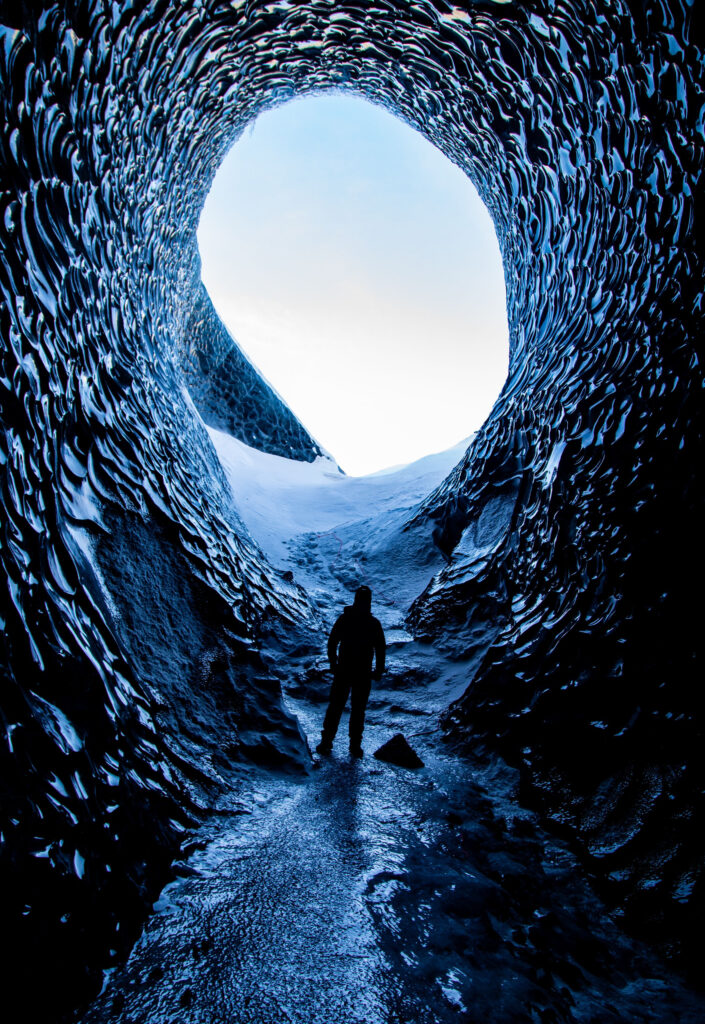 Person walking through blue caves in Iceland where tour guides allow people to safely explore glacial caves