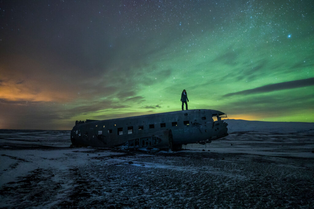 Aurora borealis dances in the night sky above the Solheimasandur Plane Crash for things to do near Vik Iceland