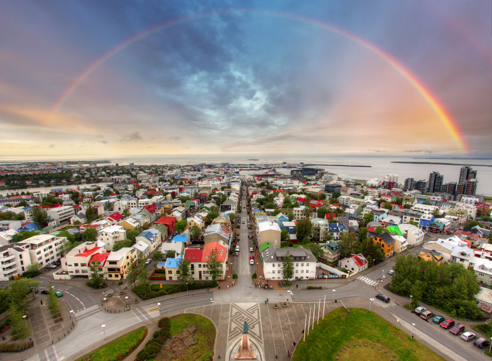 a bird's eye view of the colorful rooftops of Reykjavik with a rainbow overhead and the ocean beyond