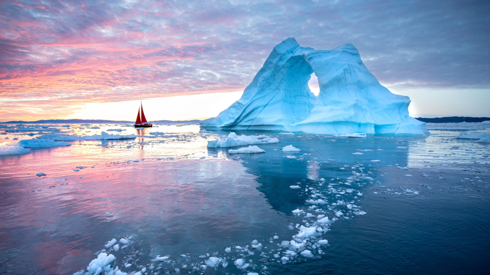 photo of greenland with an iceberg and a little red sailboat