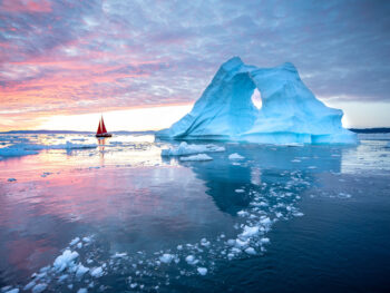 photo of greenland with an iceberg and a little red sailboat